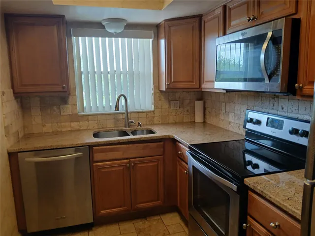 Close up of the kitchen showing the granite counter tops, stainless steel sink, dishwasher, stove, microwave and the nice window over the sink offering plenty of daylight and a sky view.
