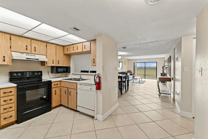 Kitchen open to living and dining area with tile flooring, pass-through window, and sliding glass door to patio