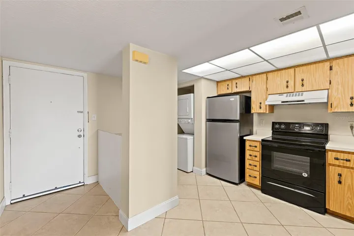 Entry foyer with in-unit stacked washer/dryer, stainless refrigerator, and kitchen view