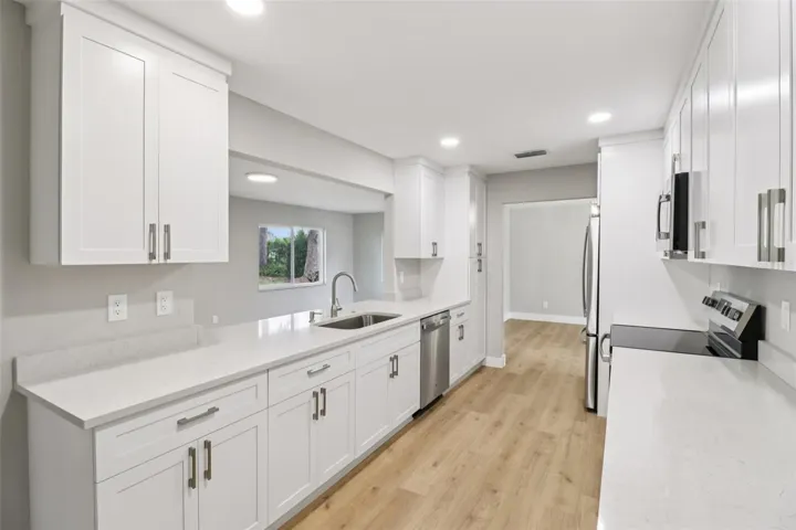 The FULLY RENOVATED KITCHEN is fresh and modern, featuring sleek stone countertops, STAINLESS STEEL APPLIANCES, ample cabinet storage, and a breakfast bar passthrough that keeps the home chef connected to the family room.