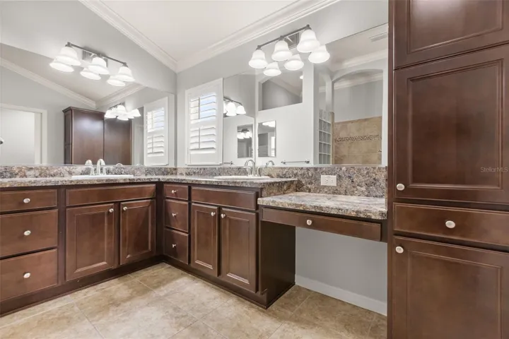 Spacious primary bath featuring dual sinks, makeup vanity, linen cabinet, pull-out drawers, and plantation shutters.