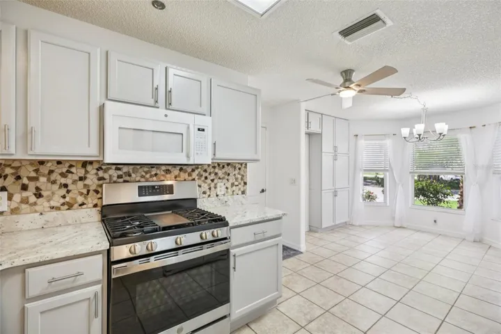 The kitchen is designed for function and connection, featuring a STAINLESS STEEL GAS RANGE, pantry storage, breakfast bar, and a casual eat-in space set in front of a bright bay window, plus room for a second refrigerator if desired.