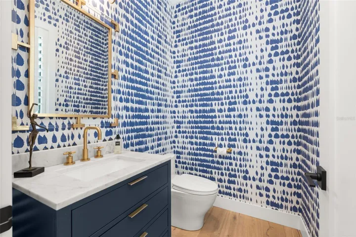 Powder bath featuring striking blue patterned wallpaper, custom vanity, and elegant Emtek brass fixtures