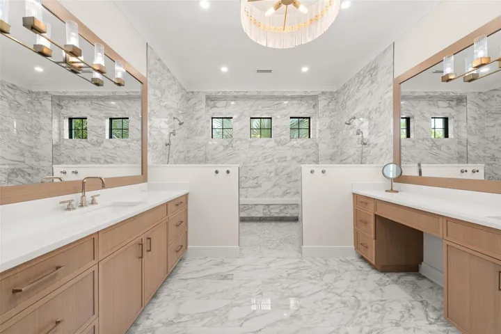 Luxurious spa-inspired primary bath featuring dual vanities, custom cabinetry, and designer lighting. The stunning marble shower with dual showerheads and built-in bench creates a serene retreat