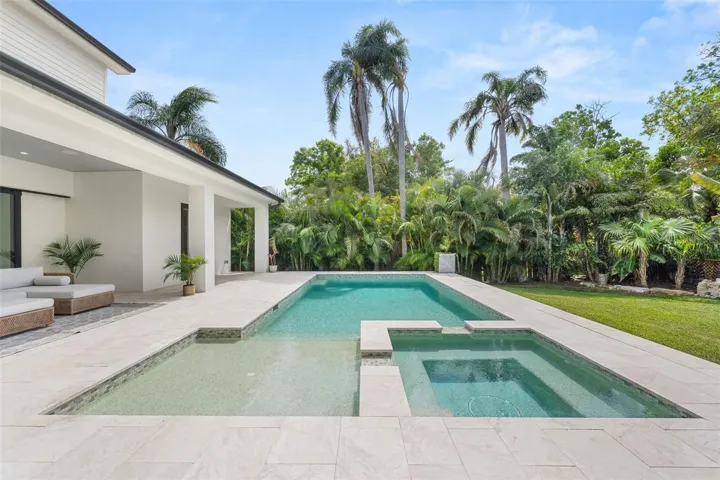 Sparkling pool and spa with a sun shelf and expansive travertine deck