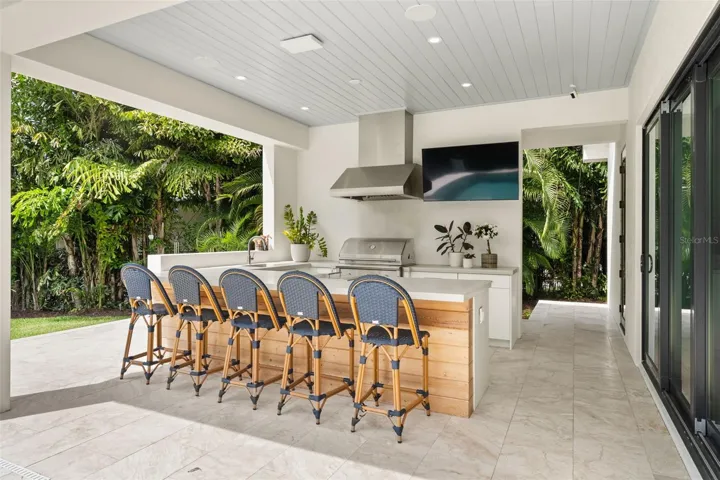 Fully equipped outdoor kitchen with bar seating, built-in grill, vent hood, and sink—perfectly designed for effortless outdoor entertaining and enjoying the Florida lifestyle