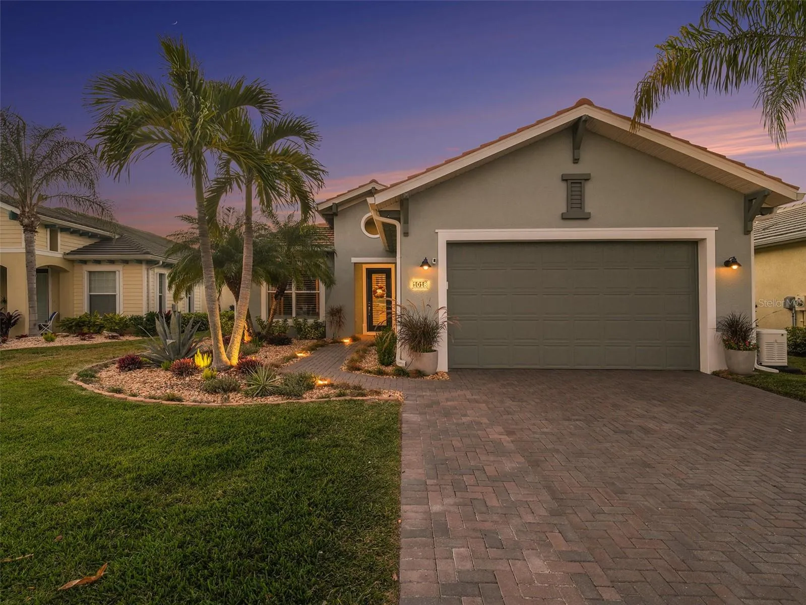 Inviting front exterior with tropical landscaping, a paver driveway, and impressive curb appeal.