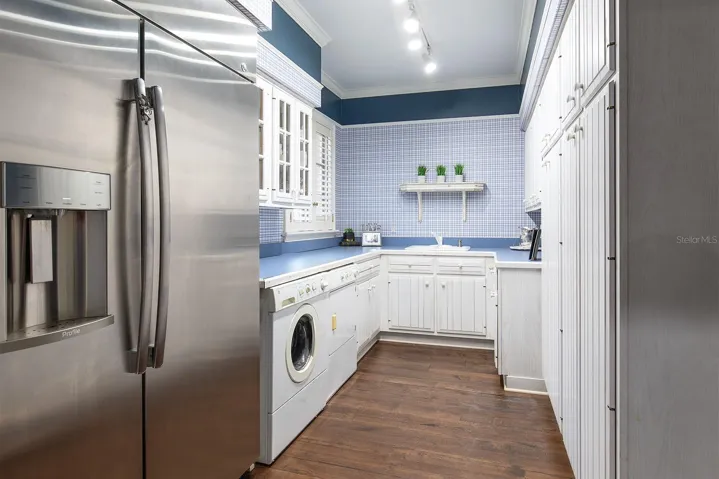 Look at the size of this laundry room! Situated off the corridor of the side entrance.  Equipped with an additional refrigerator, load of cabinetry and plenty of counter space for folding clothes and storage.