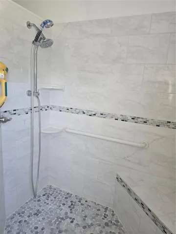 Interior of roll-in shower, hand held shower head and bench seat.