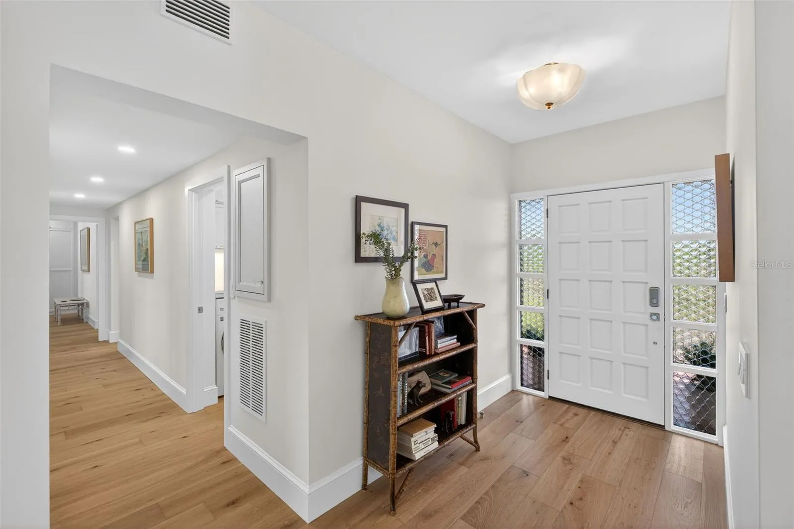 A welcoming, light-filled entry sets the tone with clean lines and warm wood floors, while the new raised panel Fir wood door &amp; glass-paneled sidelights invite in soft natural light and offer a glimpse of the greenery beyond—creating an inviting first impression that flows effortlessly into the home’s airy interior.