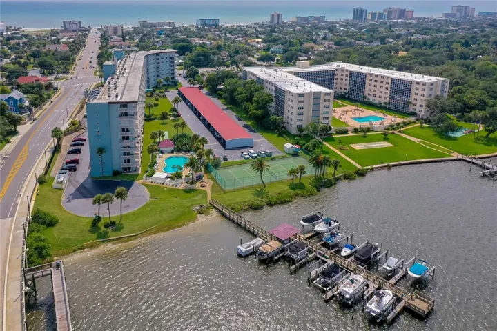 Expansive aerial perspective showcasing the community’s private dock, waterfront setting, pool, and tennis court, all just moments from the beach.