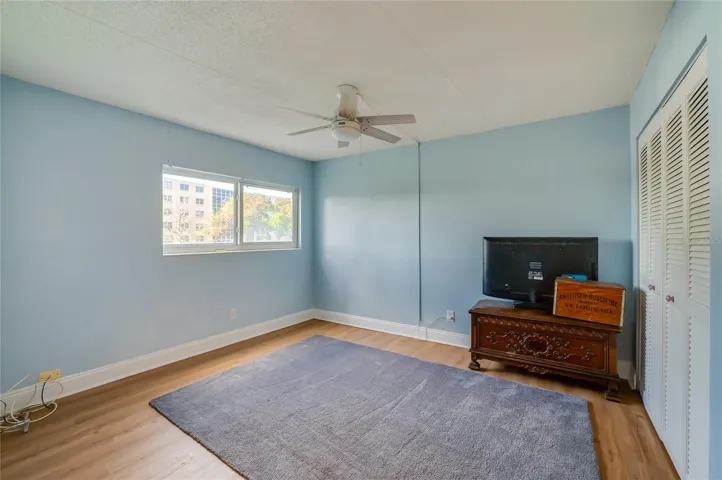 Versatile bedroom with a large window, ceiling fan, and ample floor space, suitable for a variety of uses.