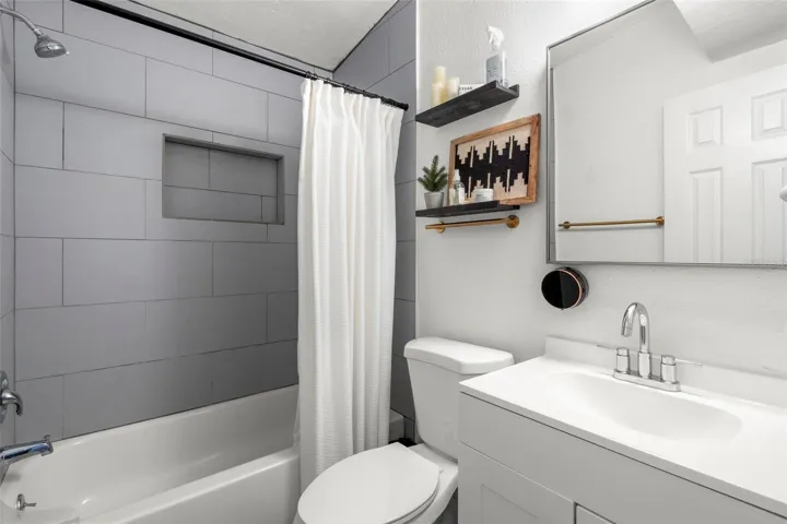 Updated bathroom with modern mirrored vanity with storage  and oversized tile surround.