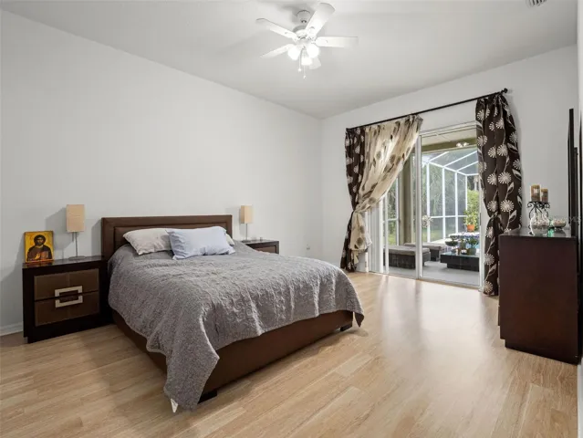 Spacious and light-filled primary suite featuring vaulted ceilings, wood-style flooring, and direct access to the covered lanai through sliding glass doors. A serene retreat with seamless indoor-outdoor flow.