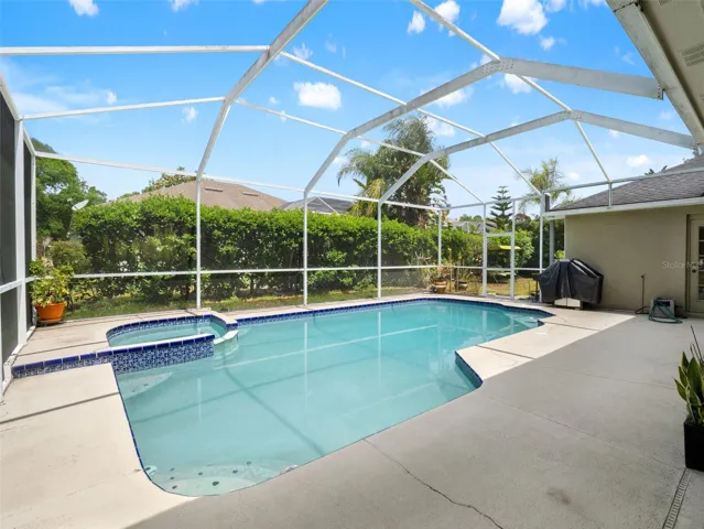 Inviting pool with attached spa, enclosed by a screened cage and bordered by lush greenery for added privacy.