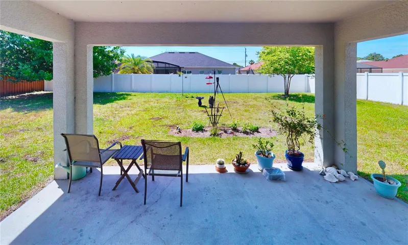 Covered lanai with a relaxing view of the fully fenced backyard—an easy spot for morning coffee, grilling, or unwinding outdoors with added privacy.