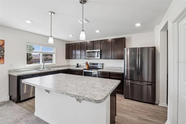 The kitchen offers a comfortable, functional design with rich cabinetry, STAINLESS STEEL APPLIANCES, plenty of counter space, and a large ISLAND with bar seating and pendant lighting.