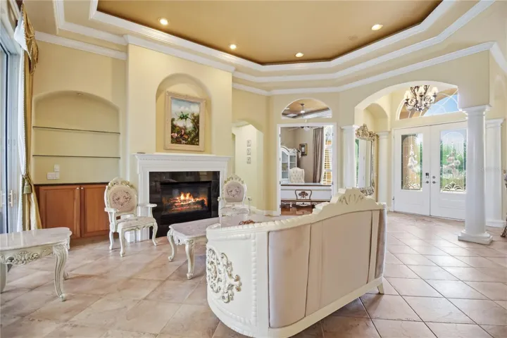 Formal living room with fireplace, architectural columns, and pool views.