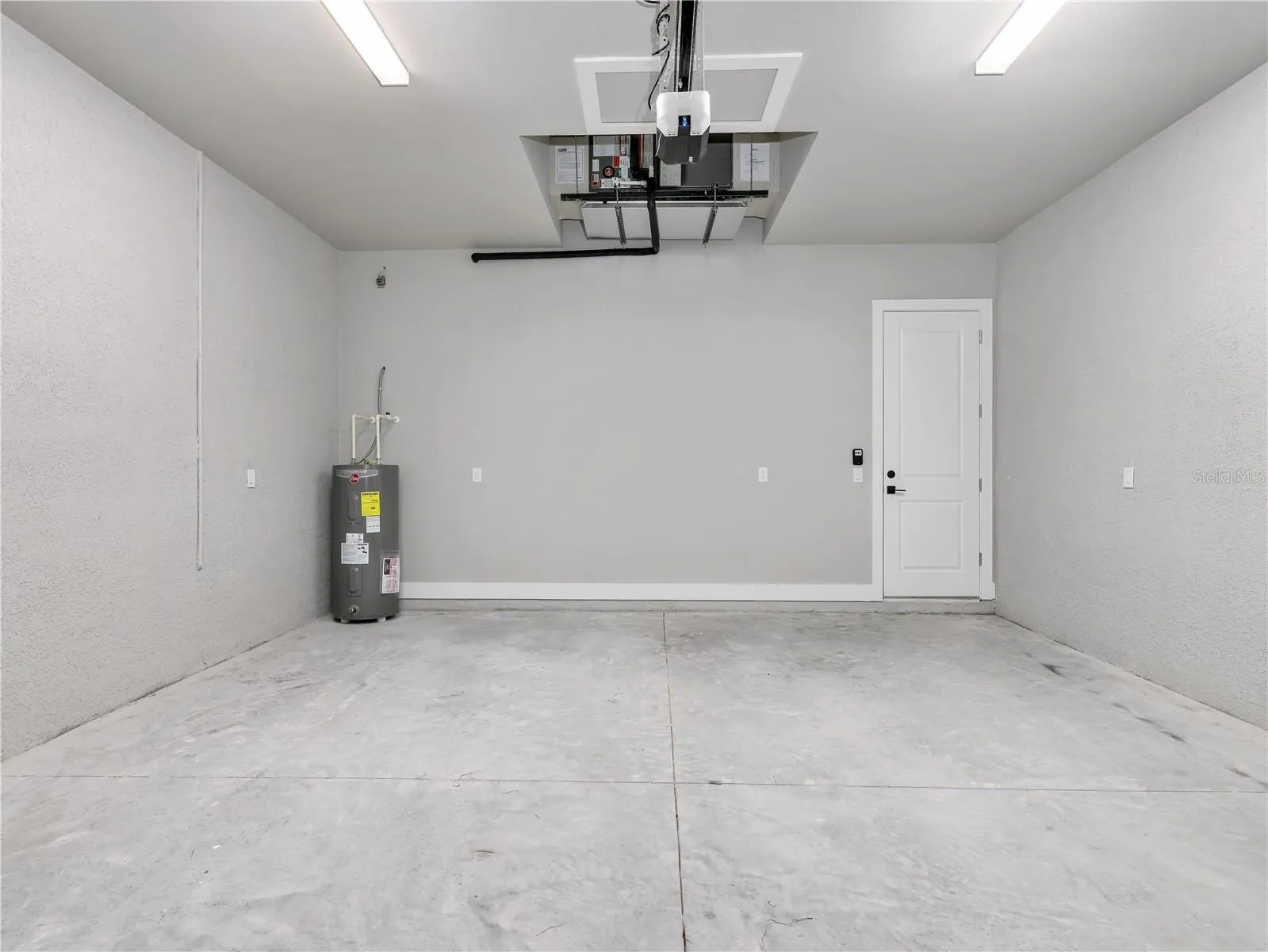Spacious garage featuring concrete flooring, a water heater, and an overhead garage door opener mechanism