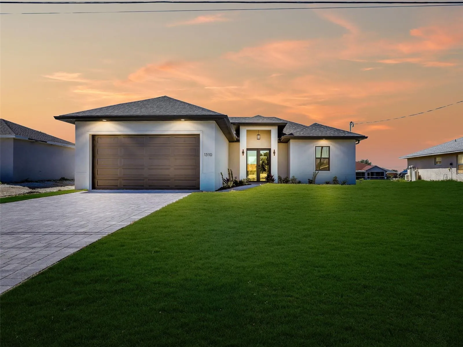 Contemporary stucco exterior with a darkbrown garage door, dark shingle roof, and apaved driveway the color of the grass has been virtually enhanced