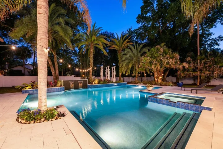 The oversized saltwater pool features a waterfall, two fountains, and a heated spa, while the backyard is fully enclosed by concrete block and stucco wall fencing for a rare level of privacy.