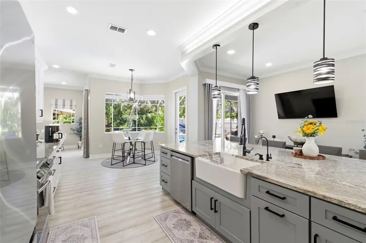 Stunning open-concept kitchen designed for both everyday living and entertaining, featuring a large center island with farmhouse sink, granite countertops, and ample cabinetry. Modern pendant lighting, stainless steel appliances, and sleek finishes create a clean, contemporary look. The space flows seamlessly into a bright dining area with large windows overlooking the pool and lush landscaping, while sliding glass doors provide easy indoor-outdoor living.