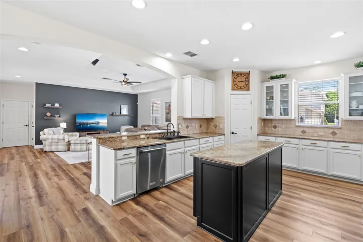 The CHEF-INSPIRED KITCHEN is truly a centerpiece, beautifully updated with RESURFACED CABINETRY with NEW HARDWARE and PULL-OUT SHELVING (2024), glass-front accents, granite countertops, a sleek tile backsplash, stainless steel appliances (including a NEW REFRIGERATOR in 2025), a center island, breakfast bar, and pantry closet.