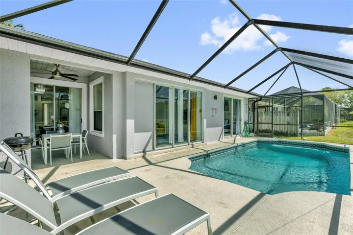Rear exterior view highlighting the screened pool, covered lanai, and multiple access points to the home
