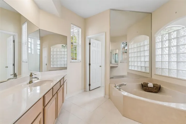 Primary suite overlooking the pool, featuring two closets and an ensuite bathroom with dual vanities, a walk-in shower, a garden tub, and a private water closet