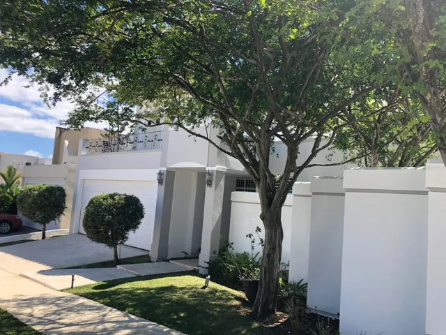 Corner-lot residence with enhanced privacy, featuring lush tropical landscaping and a spacious driveway. The home’s unique architecture and mature trees create a welcoming and upscale residential setting in Mansiones Reales, Guaynabo.
