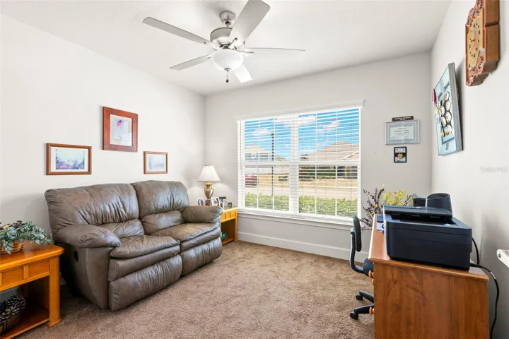 Bedroom 2 offers flexibility for guests, family, or a home office, featuring neutral finishes, plush carpeting, a ceiling fan, and a large front-facing window that brings in abundant natural light.