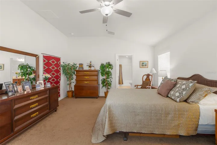 The generous primary bedroom features vaulted ceilings, a ceiling fan, neutral tones, and direct access to the ensuite bath.