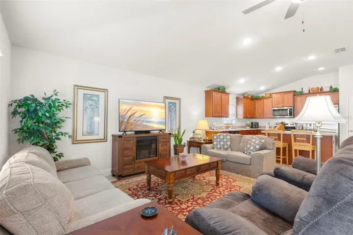 Open sightlines connect the living area to the kitchen, where warm wood cabinetry, recessed lighting, and bar seating create a functional and inviting central gathering space.