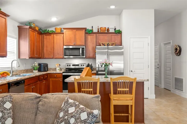The open kitchen features warm wood cabinetry, stainless steel appliances, granite-look countertops, a center island with bar seating, dual sinks, a closet pantry and generous prep and storage space.