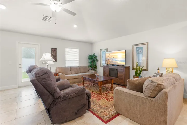 The spacious living room offers neutral tones, oversized tile flooring, recessed lighting, and a ceiling fan, with airy proportions and direct access to the rear patio for seamless indoor-outdoor flow.