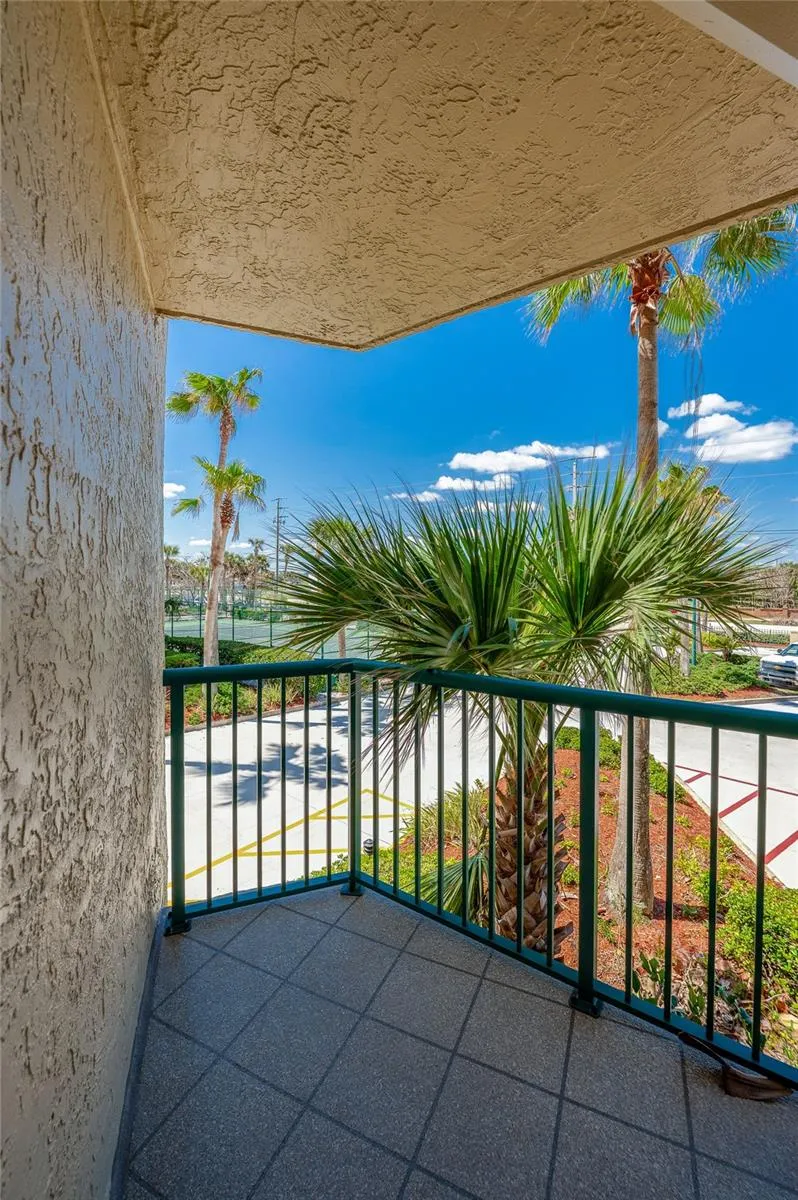 Enjoy fresh coastal air from this private balcony overlooking lush landscaping and palm trees, creating a relaxing outdoor retreat.