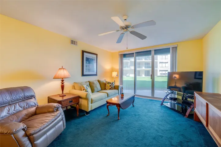 This comfortable living area features a ceiling fan, and large sliding glass doors that bring in natural light and offer direct access to outdoor views.