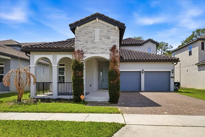 Stunning Mediterranean-style elevation with stone accents, arched entry, paver driveway, and a spacious 2-car garage.