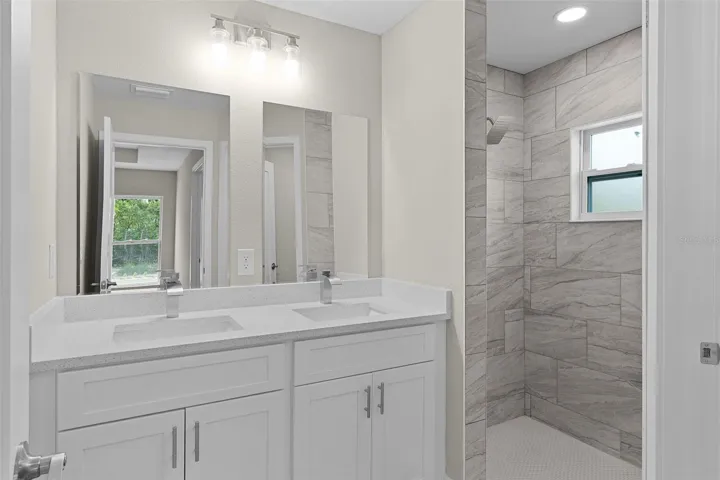Dual sinks in primary bath with tiled shower and separate toilet room