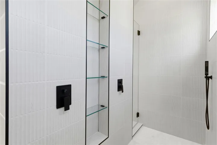 Sleek, spa-inspired walk-in shower featuring modern textured tile, frameless glass, built-in shelving, and matte black fixtures for a clean contemporary finish