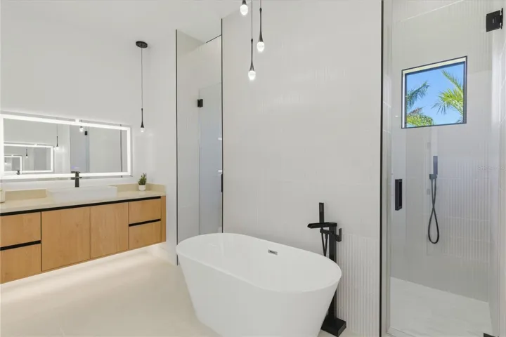Spa-like primary bathroom featuring a freestanding soaking tub, glass-enclosed walk-in shower, dual vanity with modern cabinetry, and elegant designer finishes throughout
