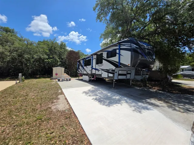 Spacious paved RV pad with full setup potential, complemented by a private storage shed and shaded surroundings for added comfort and convenience.