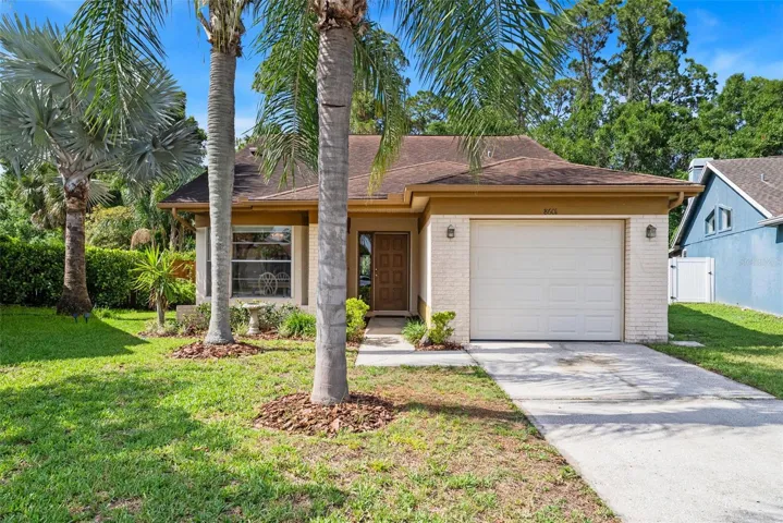 Front exterior showcasing attached garage, palms, and tropical landscaping.