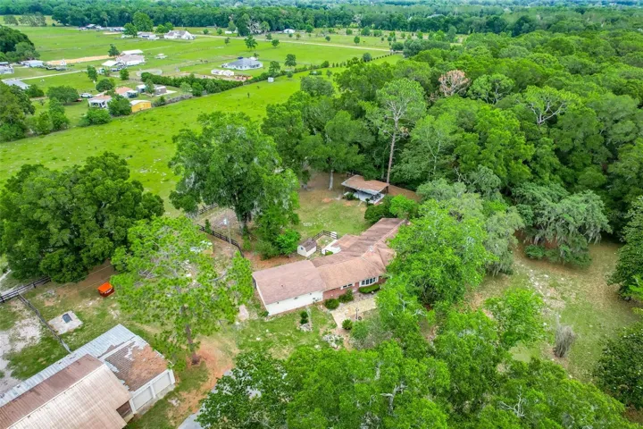 Aerial view showcasing the property’s natural beauty with a blend of wooded privacy, cleared pasture space, and the home’s peaceful setting within the 14± acres.