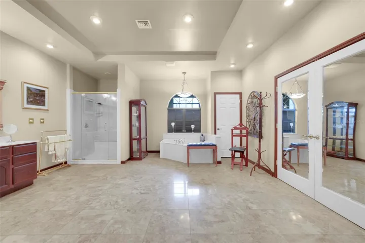 Escape to your sprawling primary bath retreat featuring impressive scale, a garden tub with atrium backdrop, separate walk-in shower, and mirrored-door acess to the expansive walk-in closet beyond.