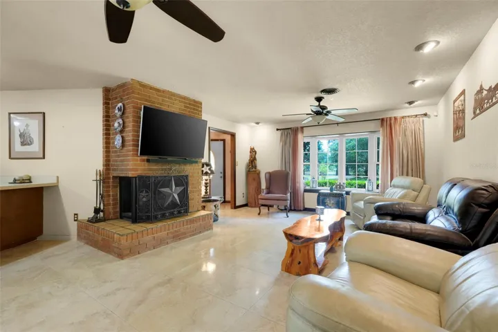 Warm and welcoming family room showcases a wood-burning brick fireplace and bow windows framing breathtaking outdoor scenery.