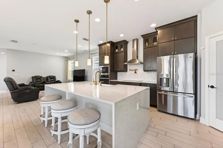 The GOURTMET KITCHEN features a range hood, GE French door refrigerator, FARMHOUSE SINK with soap dispenser and air switch, POT FILLER, stacked upper cabinetry with crown molding, and a dramatic WATERFALL ISLAND that anchors the OPEN CONCEPT living and dining spaces.