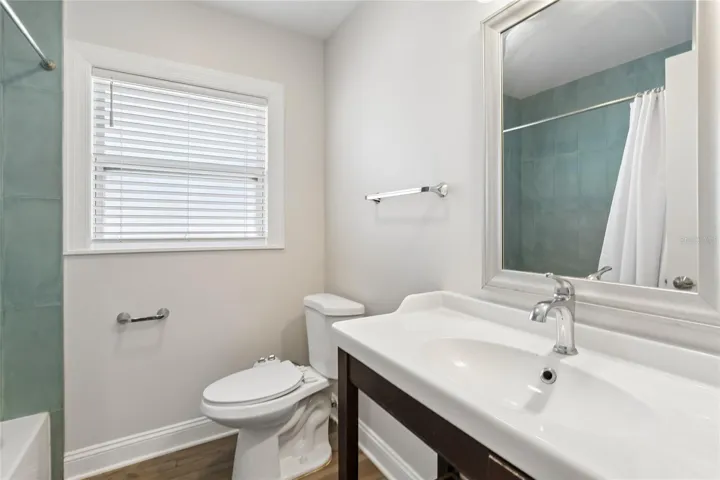 Second Bathroom – The second bathroom features a clean vanity with a framed mirror, chrome fixtures, and a window with blinds for natural light. A tub/shower combination with tile surround adds everyday convenience.