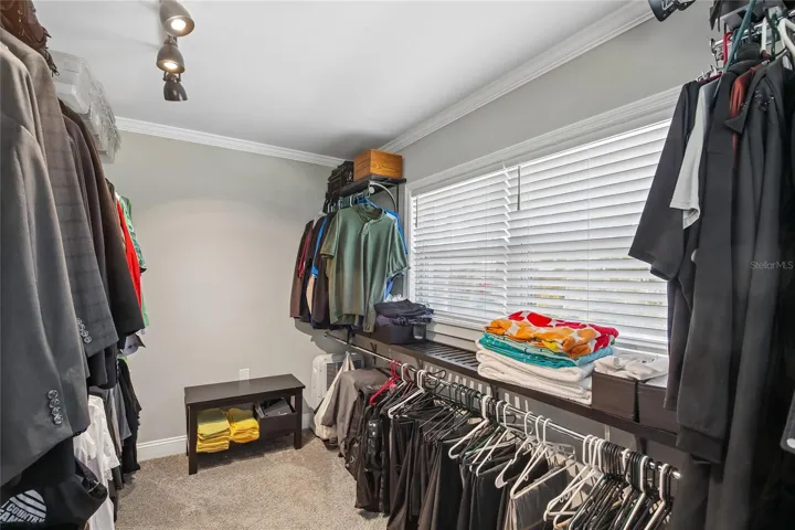 Primary Walk-In Closet – The oversized primary walk-in closet offers an impressive amount of hanging and storage space, with a wide layout, built-in organization, and a window that brings in natural light. Carpeted flooring and overhead lighting add comfort and function to this well-designed storage area.