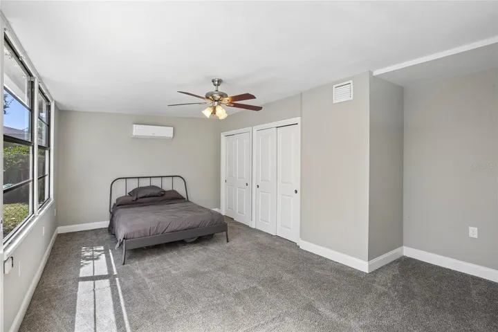 Fourth Bedroom - The fourth bedroom offers a spacious layout with plush carpeting, a ceiling fan, double-door closet, and a wall-mounted mini-split system. Located just off the bonus room by the pool, it provides flexible use as a guest room, private retreat, or additional living space.